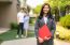 Asian confident woman real estate agent or realtor in suit holding red file and smile with young couple home sellers behind in front of house. Portrait of a lovely female broker."r
