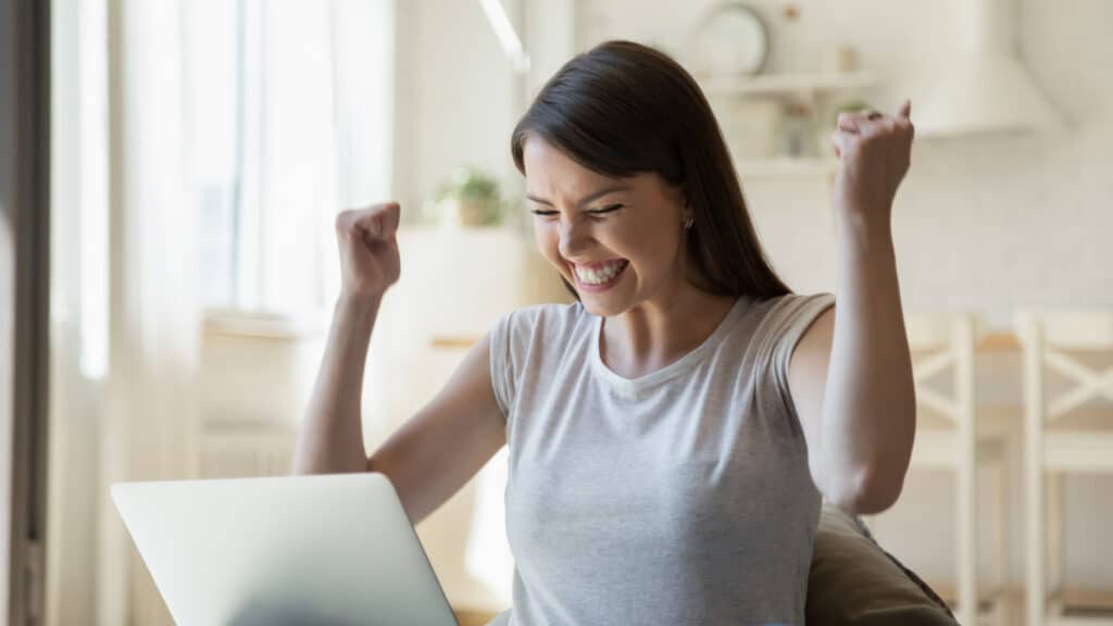 Excited young woman looking on screen of her laptop