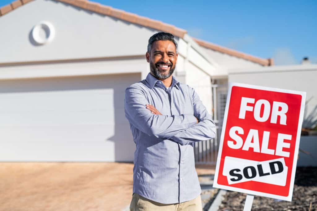 Hispanic real estate agent standing near sold sign outside house